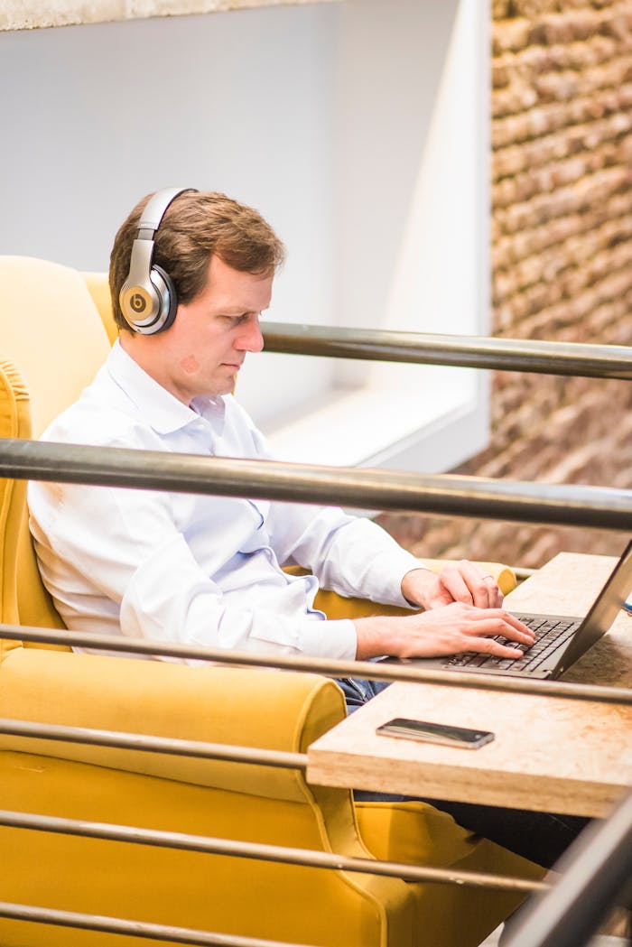 Adult man using laptop with headphones in a contemporary indoor workspace.